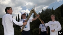 Après un hommage au fondateur des JO modernes Pierre de Coubertin, enterré près du stade d'Olympie, le Grec Spyros Gianniotis, à gauche, transmet la torche au Britannique Alexander Loukos, avant les JO de Londres, sur le site d'Olympie, en Grèce, le 10 mai 2012.