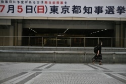 A woman walks past a banner for the gubernatorial election, displayed on the Tokyo Metropolitan Government Building, in Tokyo, Japan, July 5, 2020.