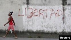 FILE - A young woman walks near graffiti that reads "Freedom" in Havana, Feb. 21, 2016. 