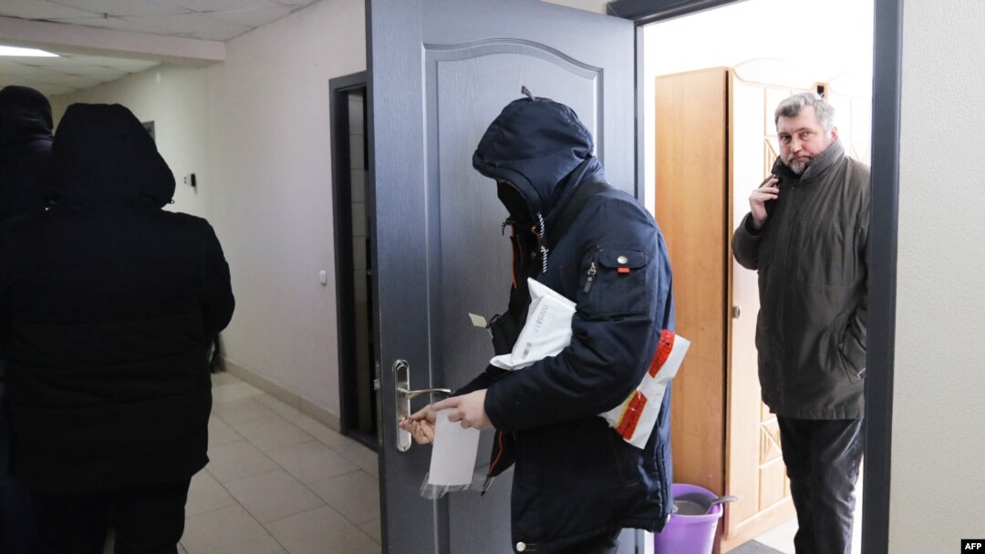 Kepala Asosiasi Jurnalis Belarusia (BAJ) Andrei Bastunets (kanan) dan polisi Belarusia meninggalkan kantor BAJ setelah penggerebekan di Minsk, Belarusia, 16 Februari 2021.