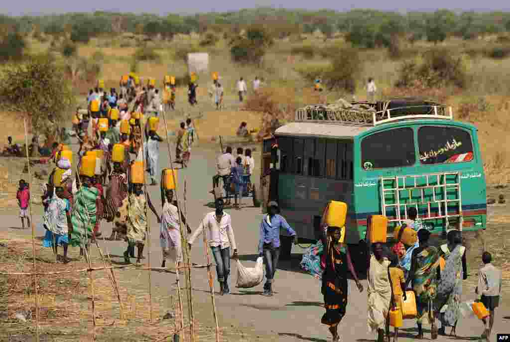 Internally displaced people carry water from outside as they walk toward the entrance of a United Nations Mission in the Republic of South Sudan base in Malakal, Feb. 6, 2014.