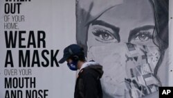 A pedestrian walks past a sign advising mask-wearing during the coronavirus outbreak in San Francisco, Saturday, Nov. 21, 2020. (AP Photo/Jeff Chiu)