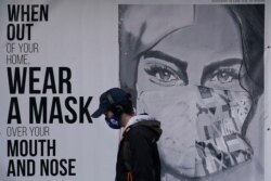 FILE - A pedestrian walks past a sign advising mask-wearing during the coronavirus outbreak in San Francisco, Nov. 21, 2020.