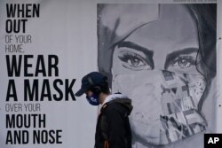 FILE - A pedestrian walks past a sign advising mask-wearing during the coronavirus outbreak in San Francisco, Nov. 21, 2020.