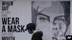 A pedestrian walks past a sign advising mask-wearing during the coronavirus outbreak in San Francisco, Nov. 21, 2020.