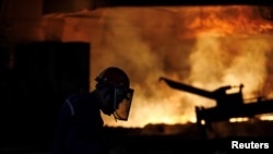 FILE - A worker is silhouetted against a blast furnace at the Chongqing Iron and Steel plant in Changshou, Chongqing, China, Aug. 6, 2018. 