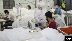 This photo taken on May 8, 2020 shows workers wearing face masks sewing disposable surgical gowns for health workers as protection from the COVID-19 coronavirus at a garment factory in Yangon. - The factory which has switched from making clothes for expor