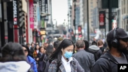 FILE - A pedestrian wears a surgical mask on a busy street as concerns grow around COVID-19, in Manhattan, New York, March 3, 2020. 