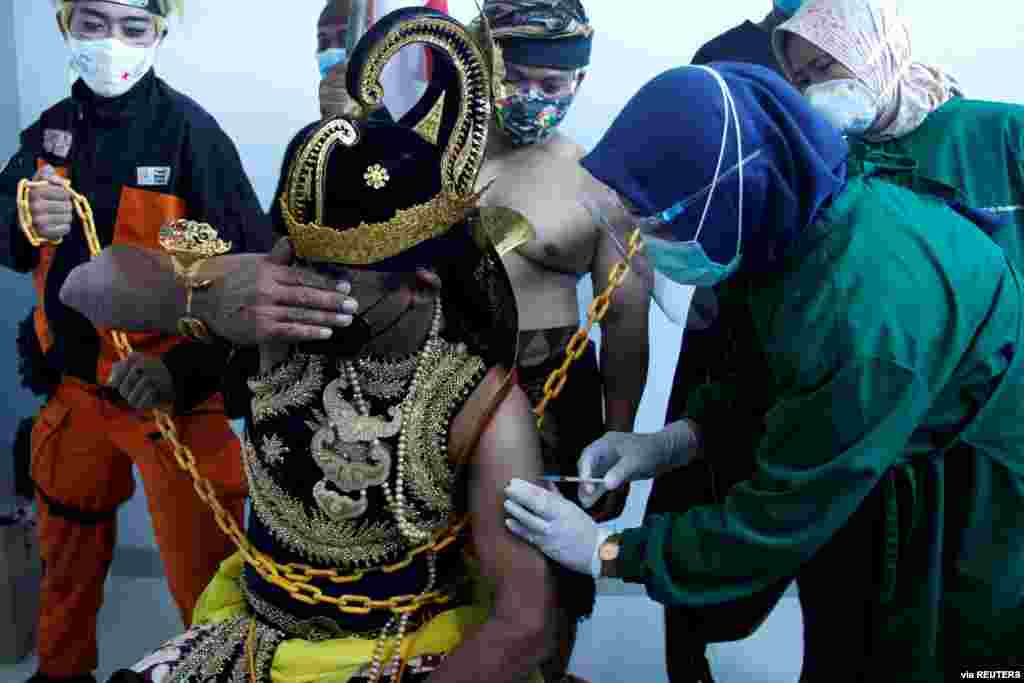 An Indonesian health care worker injects Sinovac&#39;s vaccine to a man dressed in Indonesia&#39;s traditional human puppet costume known as Wayang, as Indonesia drives mass vaccination for COVID-19, in Central Java province, Indonesia. (Antara Foto)