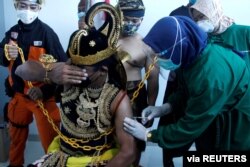 Seorang petugas kesehatan menyuntikkan vaksin Sinovac ke seorang pria yang mengenakan kostum wayang manusia tradisional Indonesia yang dikenal sebagai Wayang, di Jawa Tengah. (Foto: Antara via Reuters)