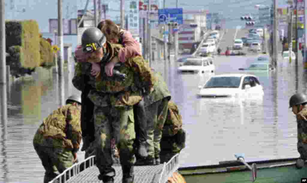 A woman is rescued from a flooded area by Japan Self Defense Forces troops in Ishimaki City, Miyagi Prefecture in northern Japan, after an earthquake and tsunami struck the area, March 13, 2011.