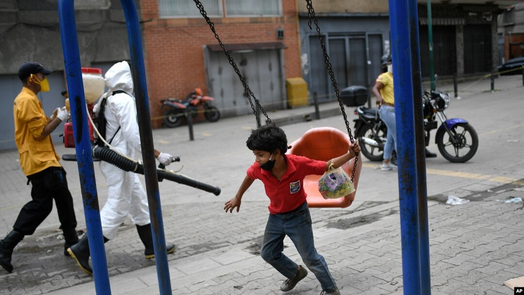 Un niño, con un tapabocas en la barbilla, juega junto a un trabajador de la ciudad que rocía desinfectante en una calle del barrio Catia, en Caracas, Venezuela.
