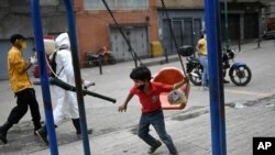 Un niño, con un tapabocas en la barbilla, juega junto a un trabajador de la ciudad que rocía desinfectante en una calle del barrio Catia, en Caracas, Venezuela.