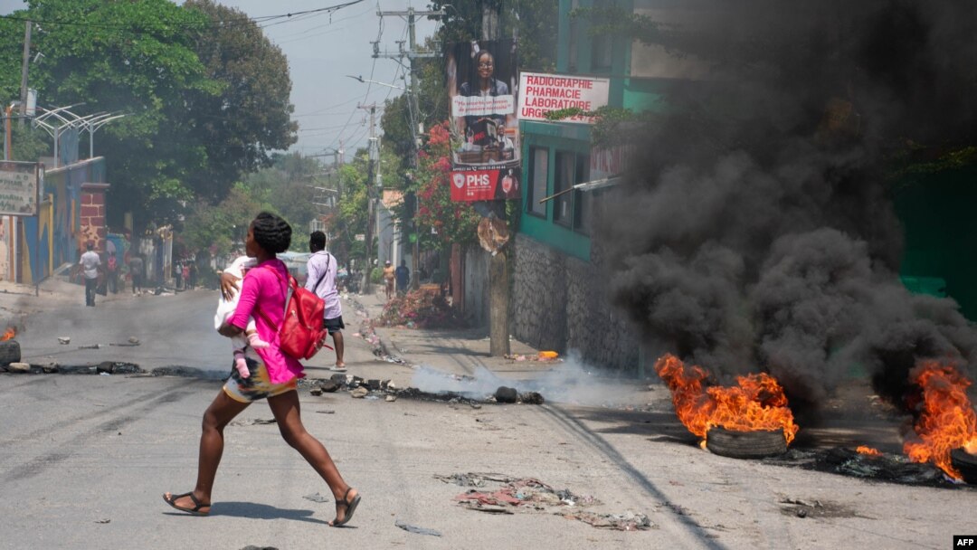 Seorang perempuan yang membawa bayi tampak berlari keluar setelah suara tembakan terdengar di kawasan Port-au-Prince, Haiti, pada 20 Maret 2024. (Foto: AFP/Clarens Siffroy)