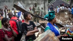 A soldier takes photos while women look at the remains of a house that was burnt down during communal violence ahead of elections in the Taouyah neighbourhood of Guinea's capital Conakry, Sep. 25, 2013. 