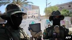 FILE - Iraqi fighters of the Shiite militia Asaib Ahl Al-Haq stand guard outside their headquarters on May 18, 2015, in the Iraqi southern city of Basra.