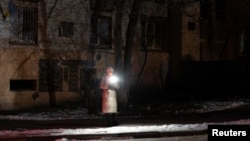 A woman holds a torch as she stands in a dark street during partial power cuts following a Russian attack on Ukrainian energy facilities, amid Russia's attack on Ukraine, in central Kyiv, Ukraine, Dec. 13, 2024.