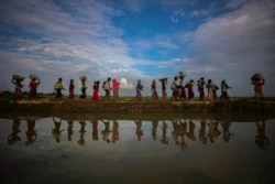 FILE - Rohingya refugees are reflected in rain water along an embankment next to paddy fields after fleeing from Myanmar into Palang Khali, near Cox's Bazar, Bangladesh, Nov. 2, 2017.
