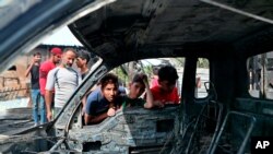 Boy look at a damaged vehicle at the scene of a powerful explosion at a crowded outdoor used furniture market in Sadr City neighborhood of Baghdad, Iraq, April 15, 2021.