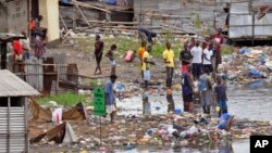 People stand on the polluted shoreline in West Point neighborhood, an area heavily effected by the Ebola virus, where residents are not being allowed to leave to prevent the spread of Ebola, in Monrovia, Liberia, Aug. 27, 2014.