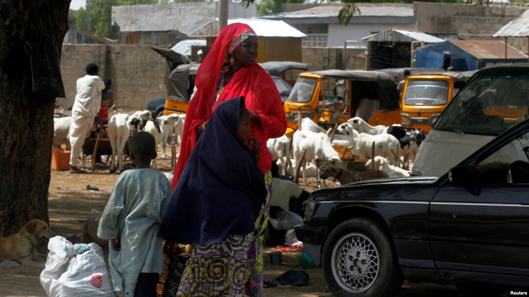 Perempuan dan dua anak menunggu kendaraan di pinggir jalan kota Maiduguri, negara bagian Borno, Nigeria, setelah militer mengumumkan jam malam (19/5). (Reuters/Afolabi Sotunde)
