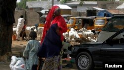 Perempuan dan dua anak menunggu kendaraan di pinggir jalan kota Maiduguri, negara bagian Borno, Nigeria, setelah militer mengumumkan jam malam (19/5). (Reuters/Afolabi Sotunde)