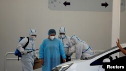 FILE - Health care workers help a woman as she is discharged from the El Salvador Hospital after surviving the coronavirus disease (COVID-19), in San Salvador, El Salvador, Jan. 19, 2021.