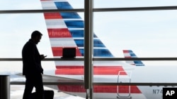 FILE - In this Jan. 25, 2016, file photo, a passenger talks on the phone as American Airlines jets sit parked at their gates at Washington's Ronald Reagan National Airport. American Airlines is giving more details on changes that will reward the…