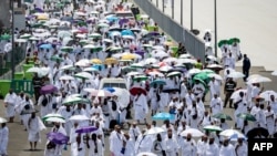 Para jemaah haji membawa payung untuk melindungi dari terik matahari, tiba di pemondokan jemaah, tenda Mina, di tengah pelaksanaan ibadah Haji di dekat Makkah, Jumat, 14 Juni 2024. (Foto: Fadel Senna/AFP)