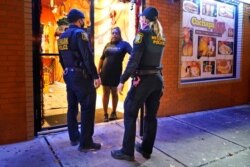 FILE - Police remind a woman in the doorway of a Newark, N.J., restaurant of the new curfew and dining regulations in an area where coronavirus cases have recently spiked, Nov. 12, 2020.