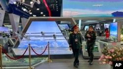 Two men in Vietnamese military uniforms walk next to a stall by Vietnamese state-owned firm Viettel at the Vietnam International Defense Expo, in Hanoi, Dec.19, 2024. 