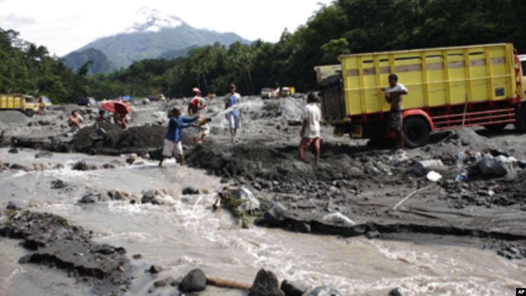 Sand miners collecting sand flowed from the eruption of Mount Merapi, as seen in the background.