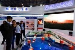 FILE - Staff members from the China National Nuclear Corporation look at models of oil tanker-shaped floating nuclear reactors and oil rigs showcased at the display booth of China's state-owned CNNC, in Beijing, April 27, 2017.