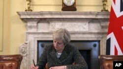 PM INggris Theresa May menandatangani surat resmi untuk pemimpin Dewan Uni Eropa, Presiden Donald Tusk, untuk pengunduran diri Inggris dari keanggotaan Uni Eropa, di ruang kerjanya di 10 Downing Street, London, 28 Maret 2017. (Christopher Furlong/Pool Photo via AP) 