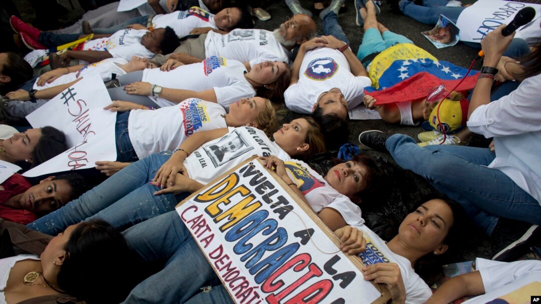 FILE - Opposition supporters lie on the ground during a demonstration outside of the Organization of American States, OAS, office building, in Caracas, Venezuela, June 23, 2016.