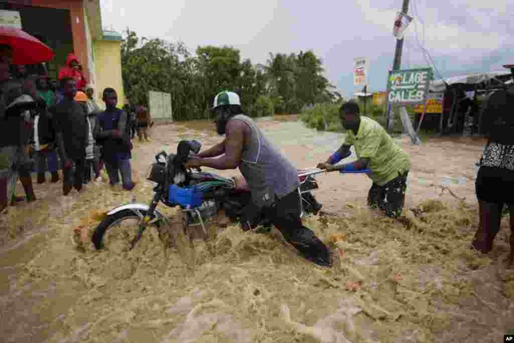 Warga mendorong sepeda motornya melalui jalan yang dibanjiri air sungai yang meluap akibat hujan lebat dari Badai Matthew di Leogane, Haiti (5/10). (AP/Dieu Nalio Chery)