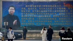 Para pengunjung berjalan di depan poster yang menunjukkan potret Presiden China Xi Jinping di Beijing, China, 26 Februari 2018.