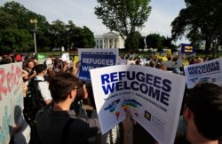 FILE - Activists hold signs in front of the White House during a rally in support of increased refugee admissions to the U.S., in Washington, June 20, 2017.