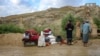 Afghan men stand beside their belongings near a damaged house after flash floods followed heavy rainfall in Firozkoh, Ghor province, Afghanistan, on May 18, 2024.