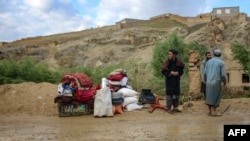 Afghan men stand beside their belongings near a damaged house after flash floods followed heavy rainfall in Firozkoh, Ghor province, Afghanistan, on May 18, 2024.