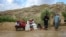Afghan men stand beside their belongings near a damaged house after flash floods followed heavy rainfall in Firozkoh, Ghor province, Afghanistan, on May 18, 2024.