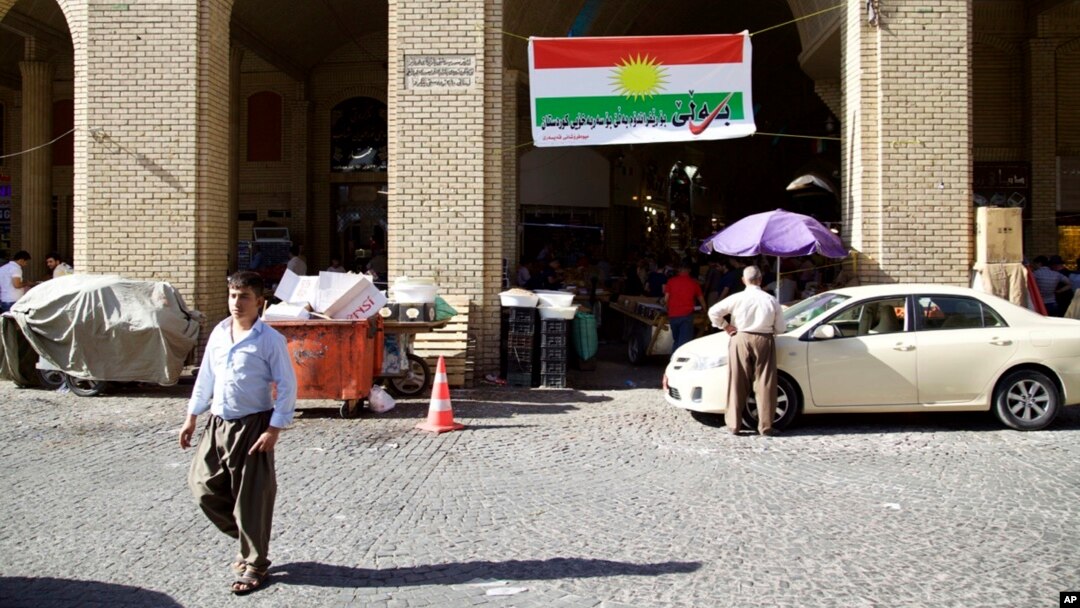 FILE - A man walks past a campaign slogan printed on a Kurdish flag urging people to vote "yes" in the upcoming poll on independence from Iraq, in Irbil, Iraq, Aug. 24, 2017.