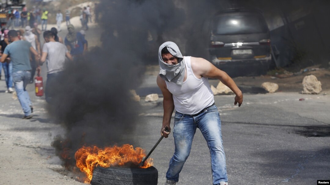 Seorang demonstran Palestina menyeret ban yang terbakar dalam bentrokan dengan pasukan Israel di kota Tepi Barat Hebron, 18 Oktober 2015. 