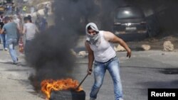 Seorang demonstran Palestina menyeret ban yang terbakar dalam bentrokan dengan pasukan Israel di kota Tepi Barat Hebron, 18 Oktober 2015. 