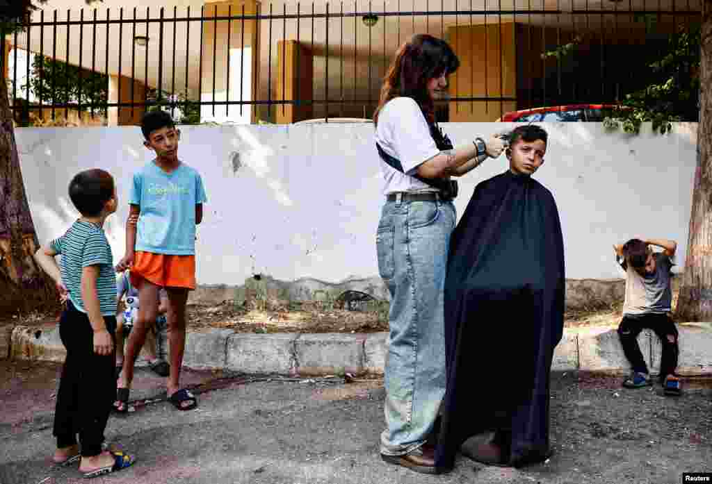 A Lebanese hairdresser who has been volunteering to give free haircuts to displaced children, cuts a child's hair outside a school used as a temporary shelter, in Baabda, Lebanon.