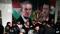 FILE - Freed Syrian detainees gather in front of posters showing Syrian President Bashar Assad, right, and his father Hafez Assad after they were released from Adra Prison, Jan. 15, 2013. A former Syrian military official who oversaw the prison has been arrested in Los Angeles.