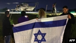 Israelis wave their national flag as a helicopter transporting newly released hostages, held by Hamas, Tel Aviv district on Nov. 28, 2023.