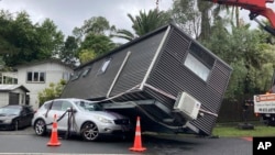 A portable building rests on a car after flood water shifted the structure in Auckland, Jan. 28, 2023.