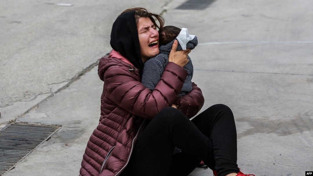 A migrant holds a child during clashes with riot police as refugees and migrants demonstrate outside the Kara Tepe camp, on the island of Lesbos, on February 3, 2020.