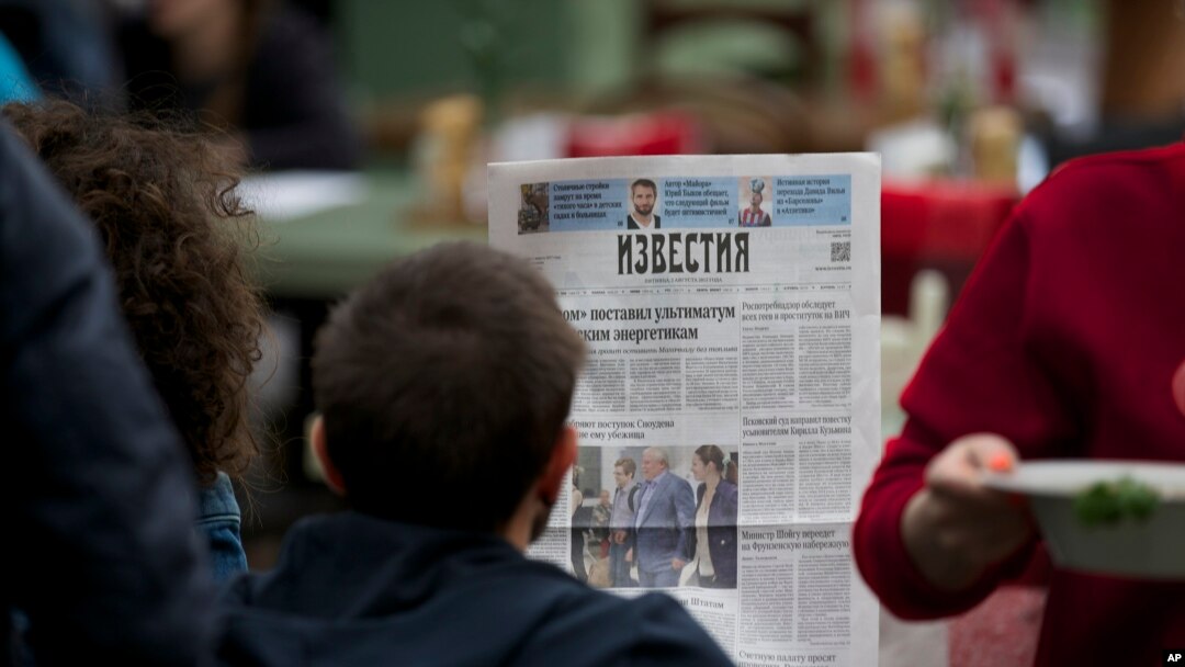 Seorang pengunjung kafe jalanan membaca koran baru Rusia "Izvestia" dengan halaman depan gambar pengacara Rusia Anatoly Kucherena, tengah, dan pembocor Badan Keamanan Nasional Edward Snowden di Moskow., sebagai ilustrasi. (Foto: AP)